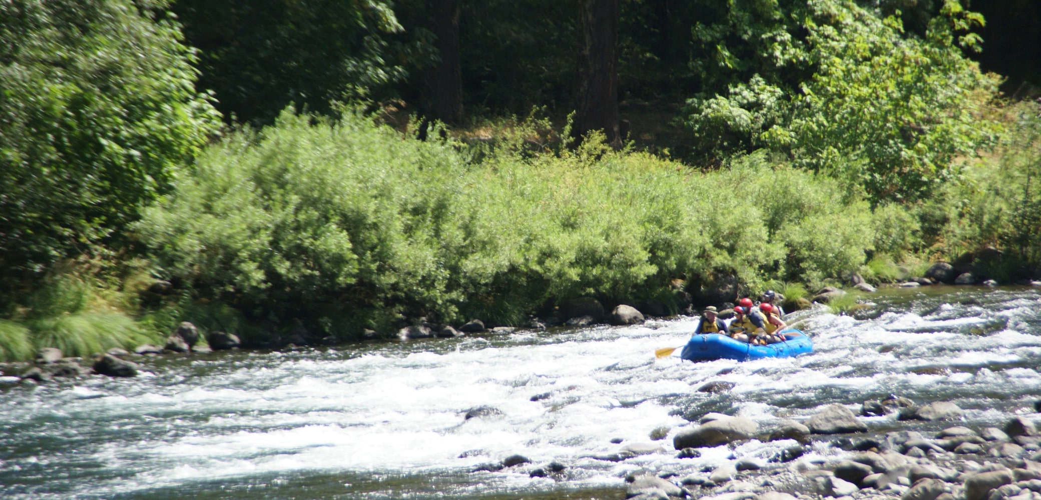 A group of white water rafters in a blue raft navigate rapids on the Sandy River.