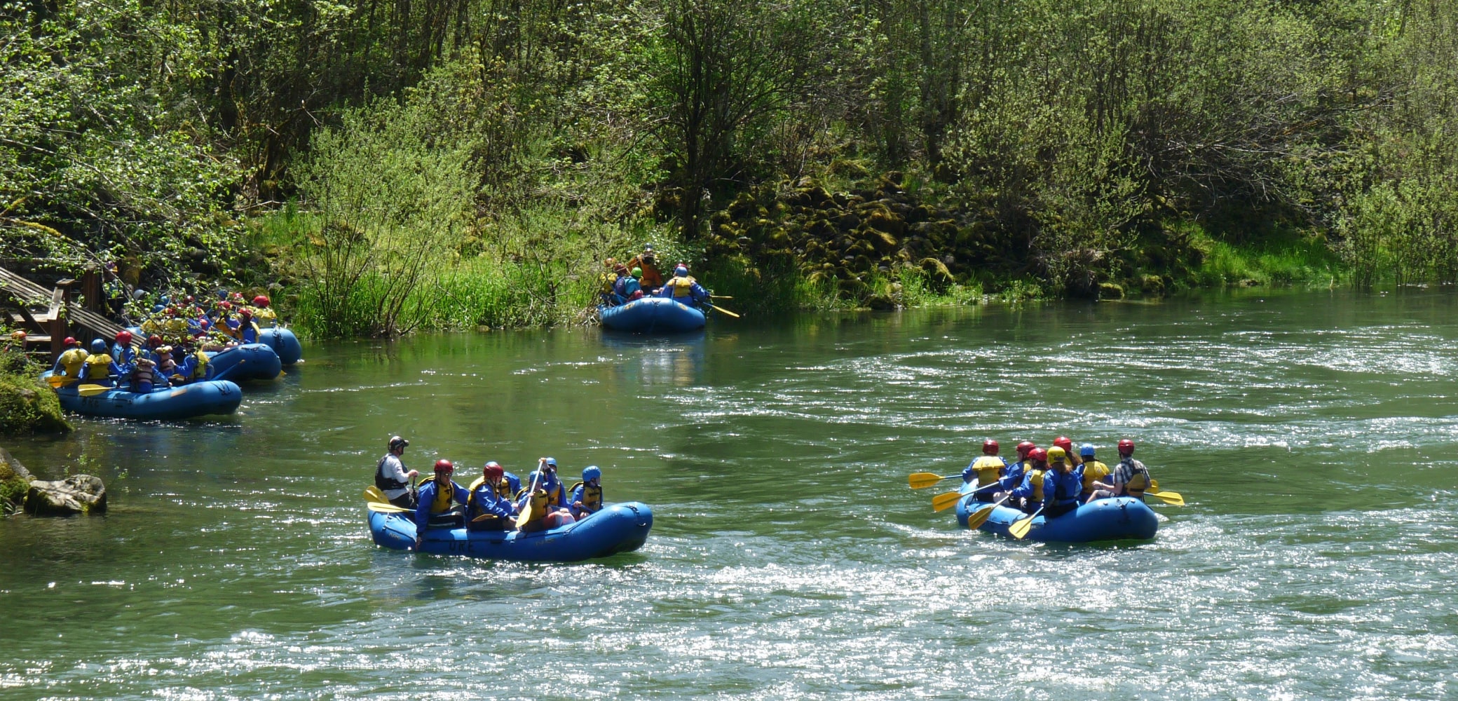Six groups of white water rafters in blue rafts take a break along the Sandy River in Oregon.