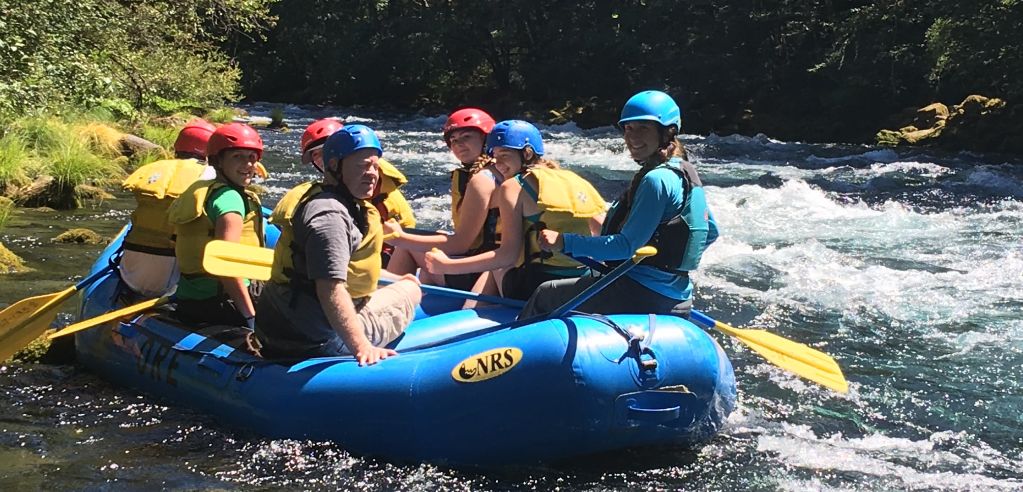 A group of seven guided white water rafters smile as they navigate rapids on the Sandy River.
