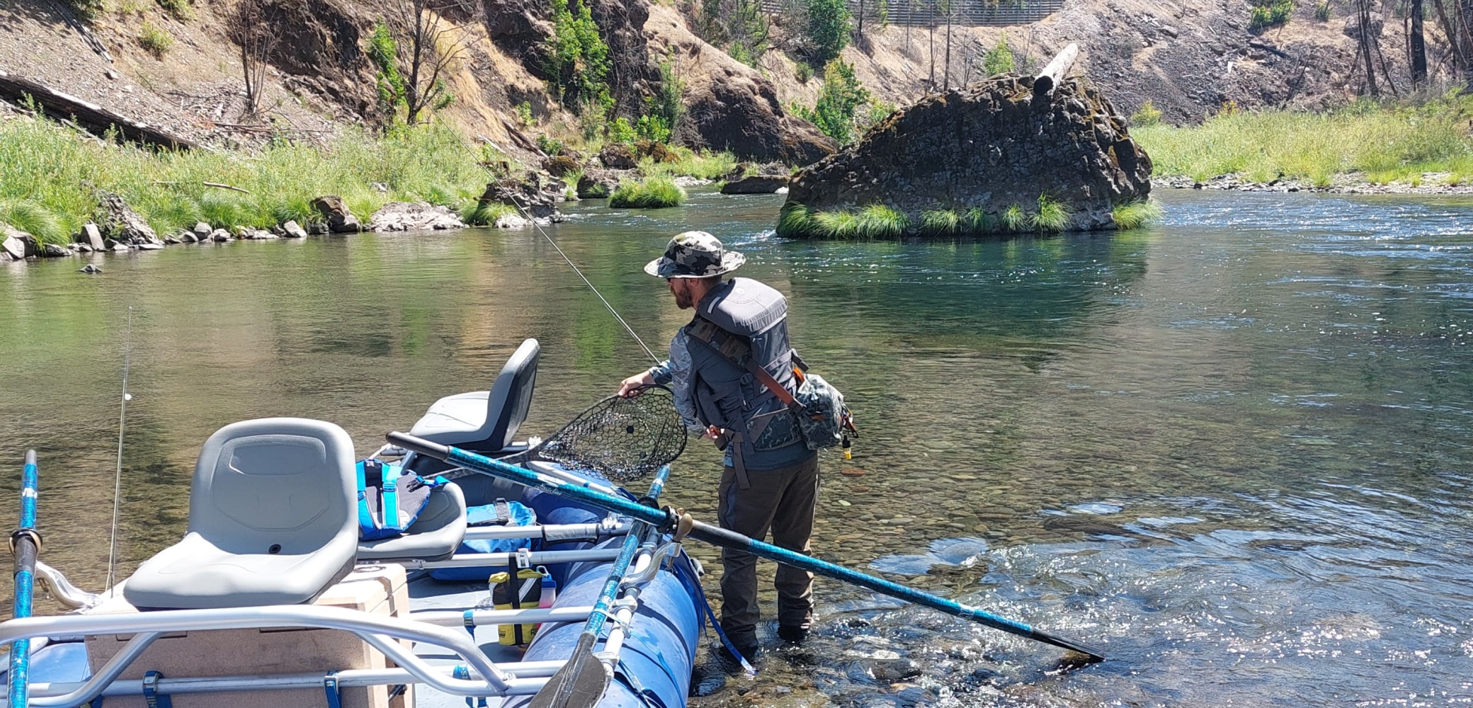 Fly fisherman grabbing a fishing net from a raft boat while on an Oregon river.