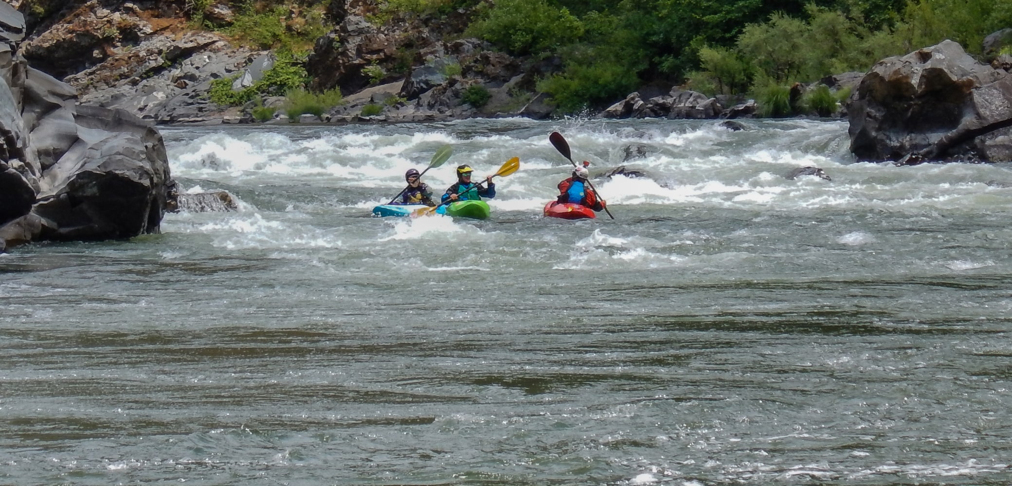 Three different kayakers navigating rapids on the Rogue River in Oregon.