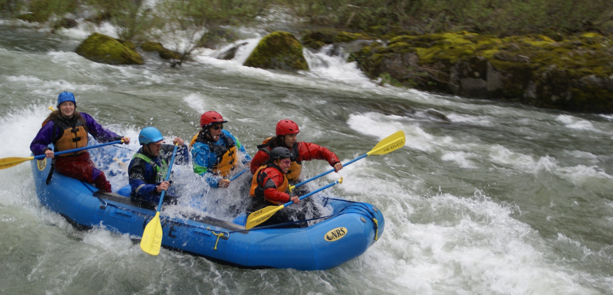 A group of 4 guided white water rafters paddle down river in Oregon