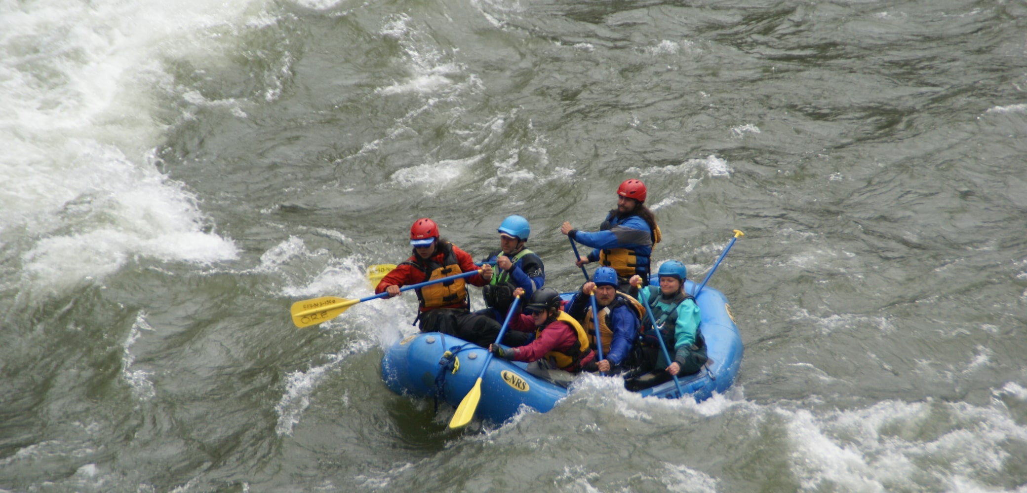 A group of 5 guided white water rafters paddle down river in Oregon.