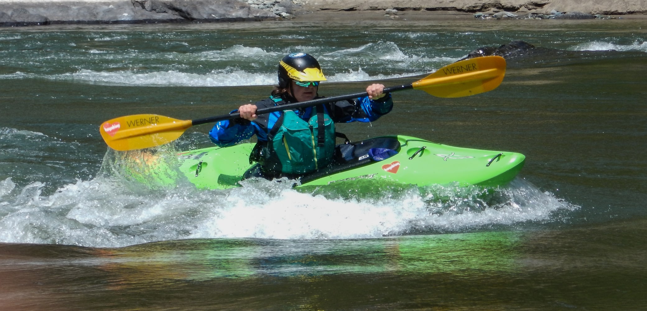 Kayaker on the Owyhee River raising their paddles above their green kayak.