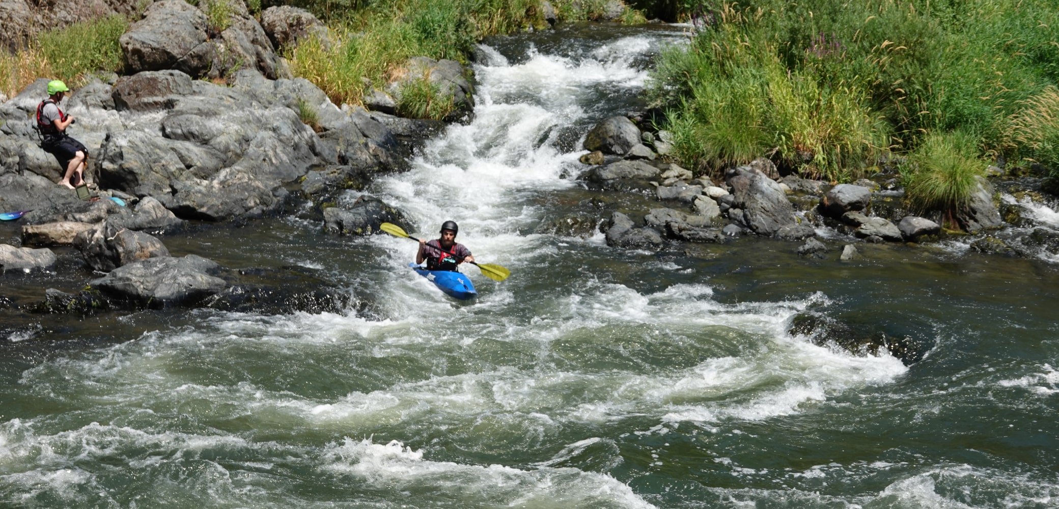 A river kayaker paddles a blue kayak down a small waterfall rapid on the Rogue River.