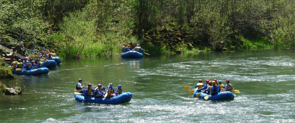 Six groups of white water rafters in blue rafts take a break along the Sandy River in Oregon.