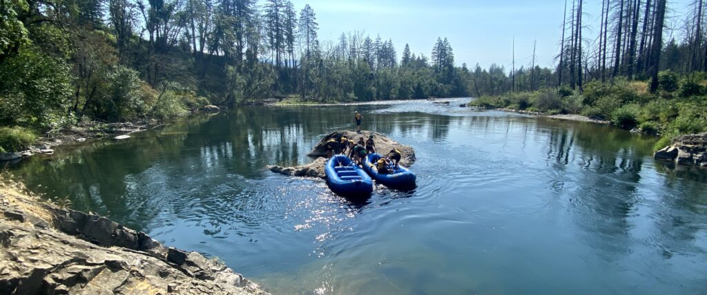 Two groups of white water rafters park their raft on a rock in the middle of the Santiam River.