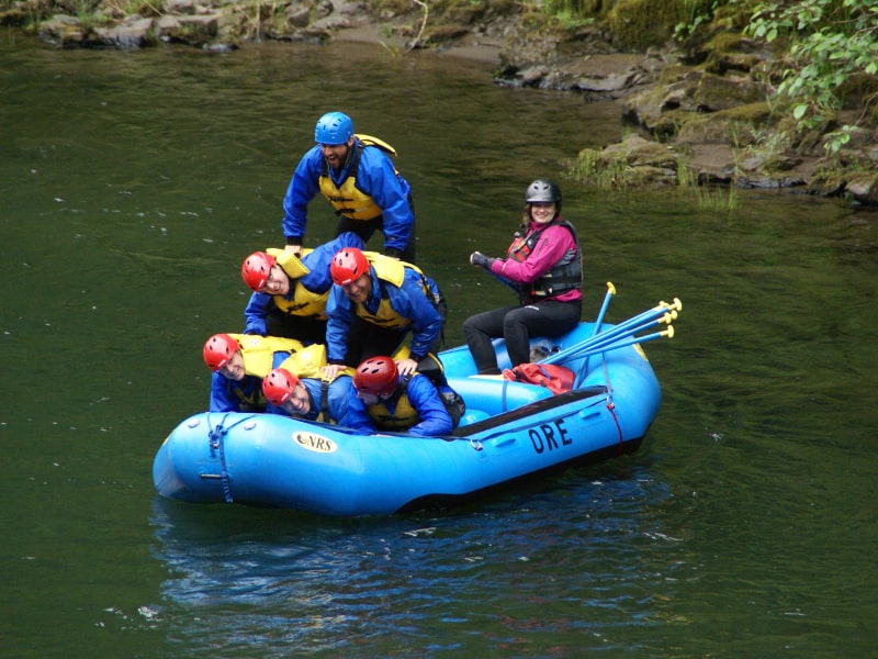 A group of river rafters making a 5 person human pyramid while on the river a blue raft.
