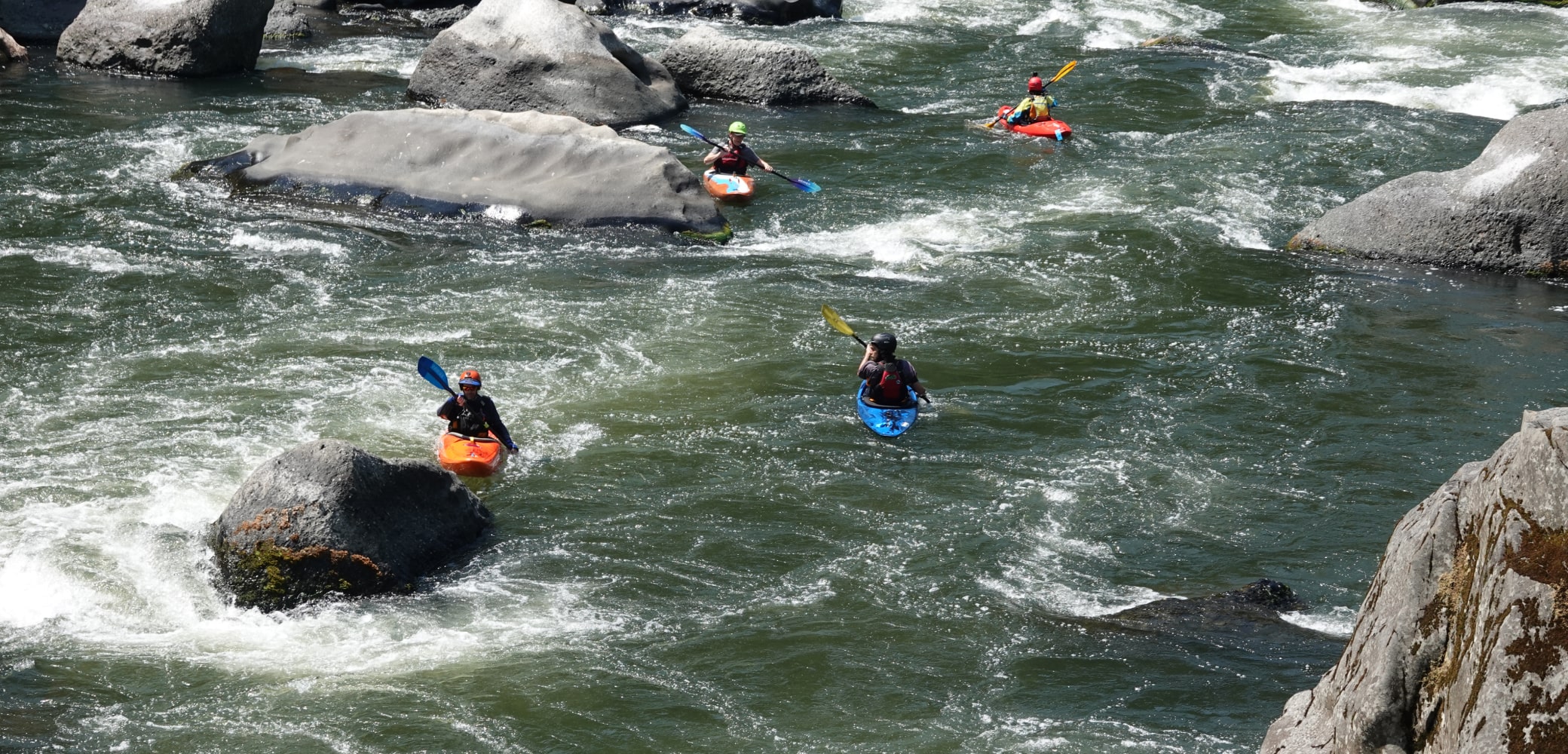 Four different kayakers navigating the Rogue River in Oregon.