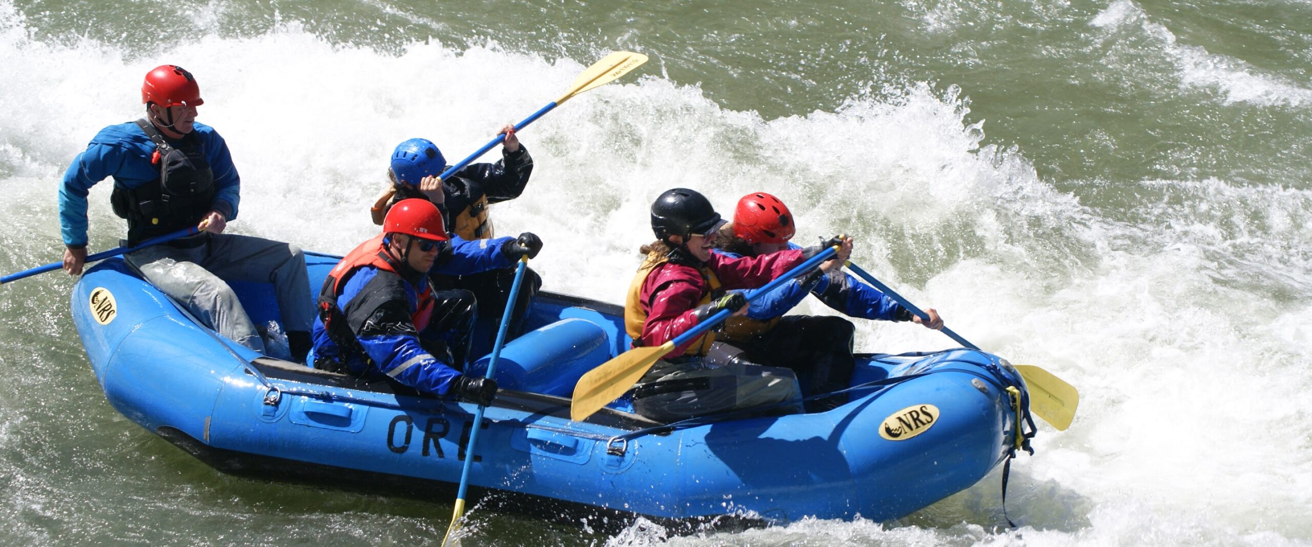 A group of guided white water rafters go through a rapid on the river in a blue raft.